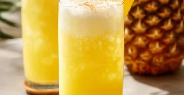 Erfrischende Ananaslimonade in einem Glas mit Eis und frischen Ananasstücken