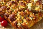 Zupfbrot mit getrockneten Tomaten, Feta und Mozzarella auf einem Holzbrett serviert.